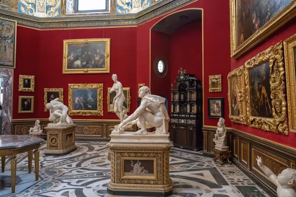 Marble statues and paintings in a red-walled room of the Uffizi in Florence.