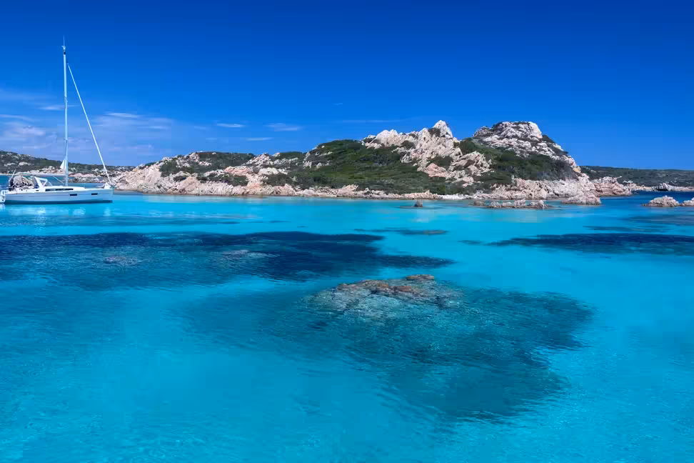 Un voilier au mouillage en eau turquoise, près d'îlots rocheux de l'archipel de La Maddalena