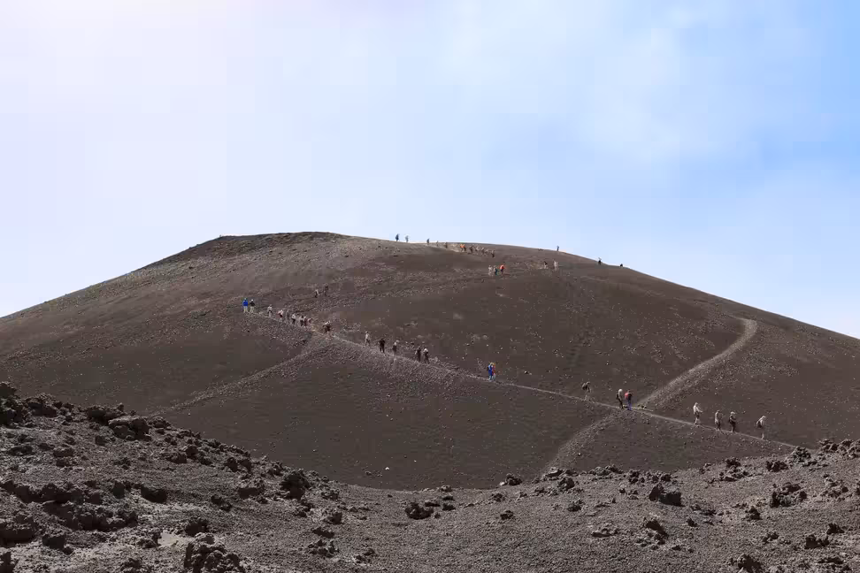 Des randonneurs en file sur une pente sombre de cendres volcaniques, sur l'Etna