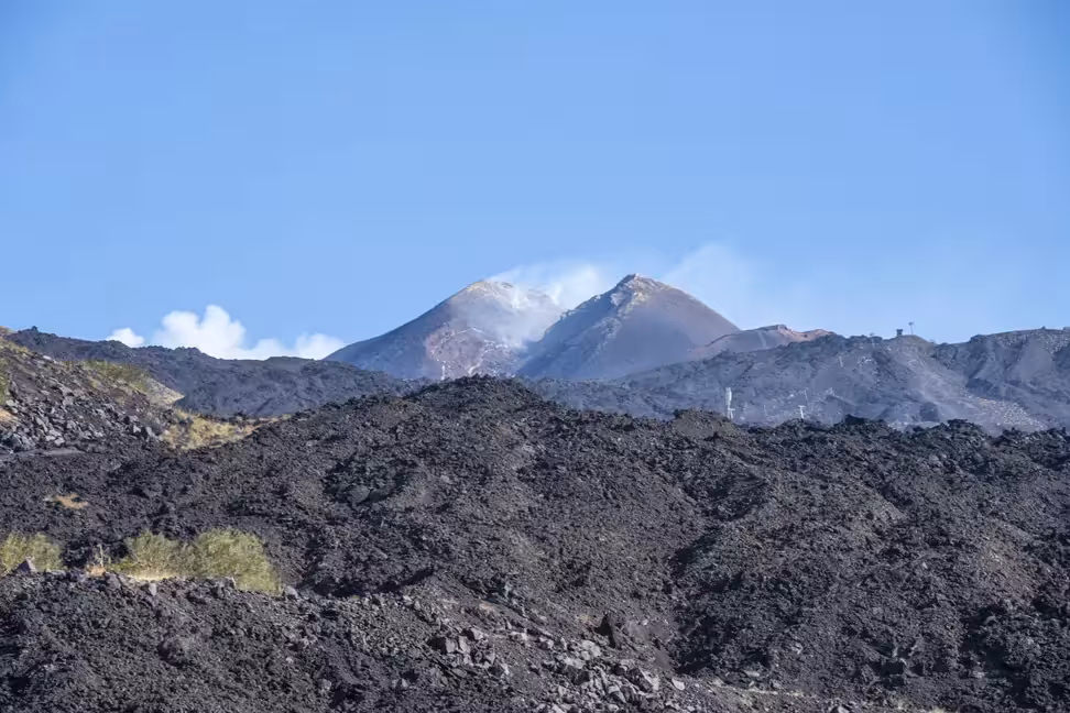 De la vapeur s'élève des cônes du sommet de l'Etna, au-dessus de champs de lave sombre