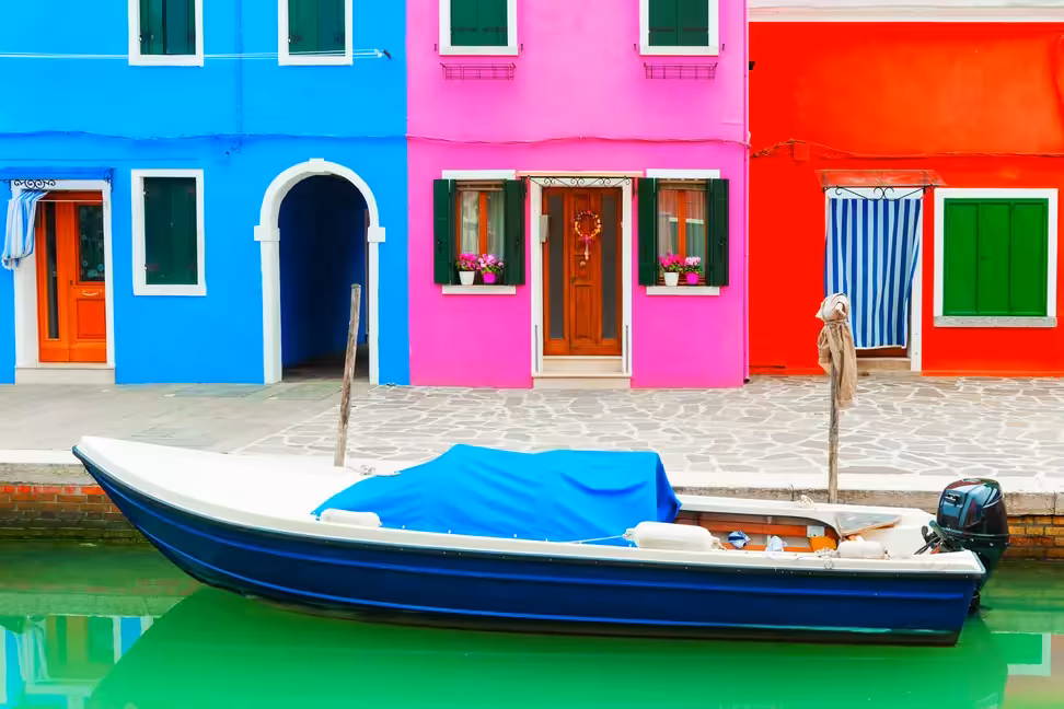 Maisons bleues, roses et rouges au bord d'un canal avec un bateau amarré à Burano