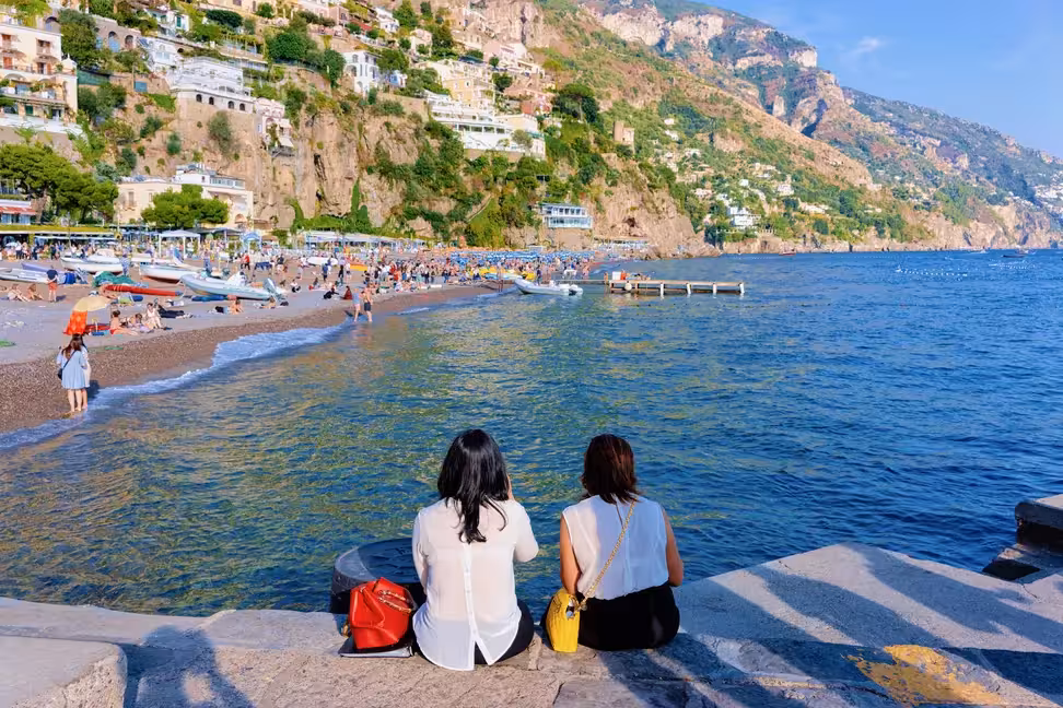 Deux femmes assises sur le muret du front de mer regardent la plage de Positano