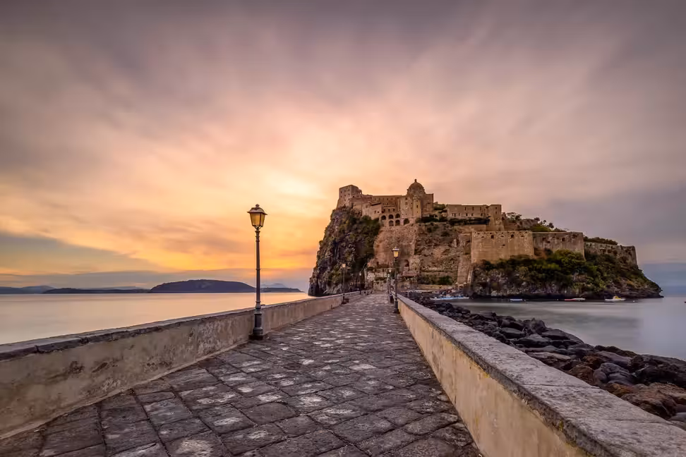 Le pont pavé bordé de lampadaires qui mène au château aragonais d'Ischia au coucher du soleil