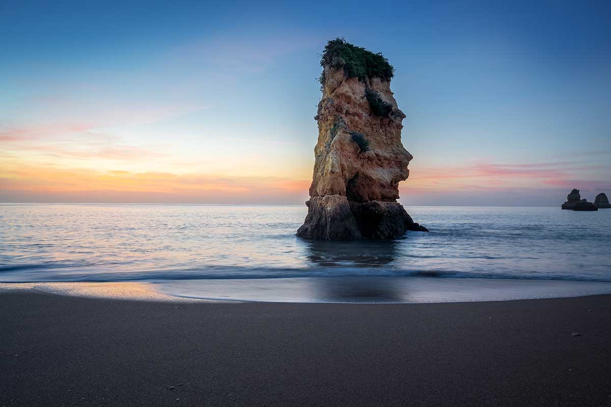 Praia de Dona Ana, nestled amidst striking limestone cliffs and turquoise waters, is a picturesque Algarve beach known for its stunning rock formations, golden sand, and clear, calm seas ideal for swimming and sunbathing.