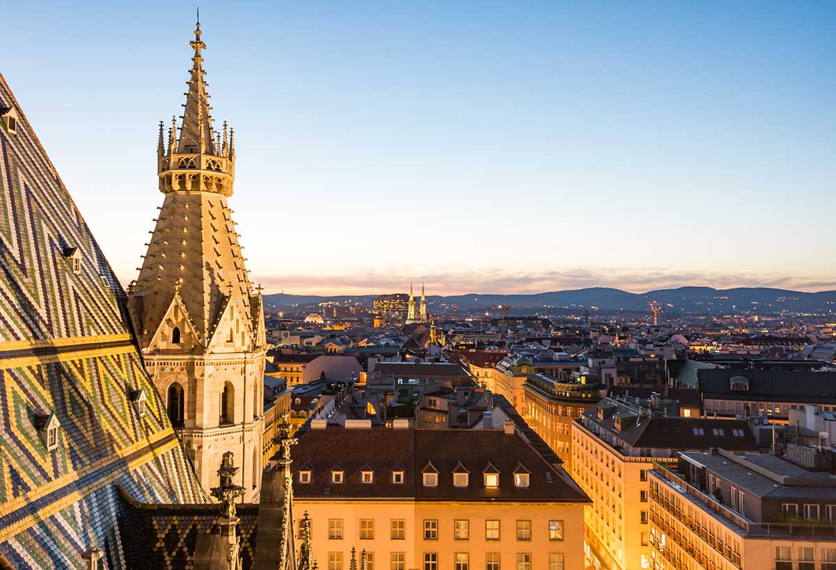 A view of Vienna at night reveals the illuminated spire of Stephansdom cathedral, a Gothic landmark, dominating the city's skyline.
