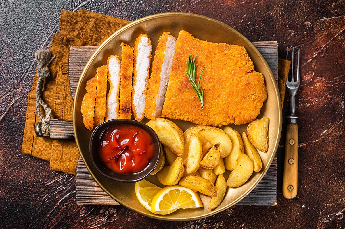 An Austrian food plate showcases a golden-brown Wiener Schnitzel, complemented by traditional sides like potato salad and lingonberry jam, highlighting the country's classic culinary flavors.