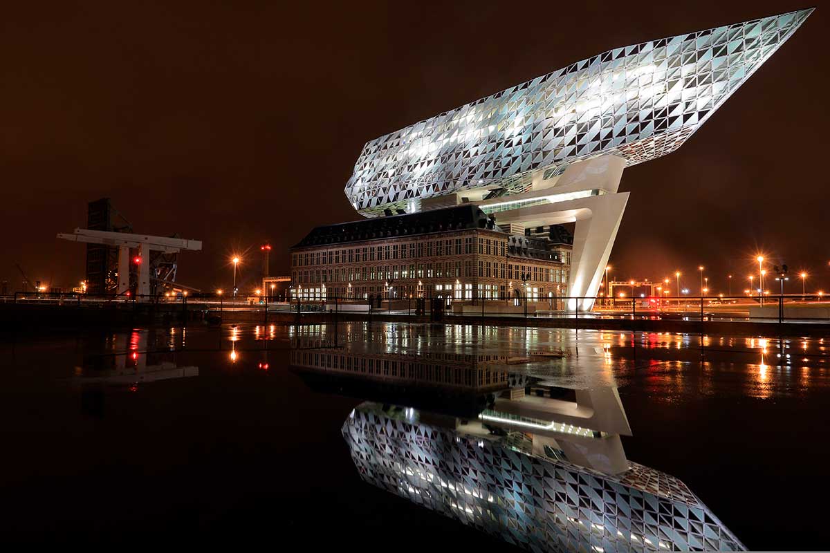 The Port House in Antwerp, Belgium, a striking modern architectural masterpiece designed by Zaha Hadid, blends a historic fire station with a futuristic glass structure, symbolizing the city's innovative spirit and maritime significance.