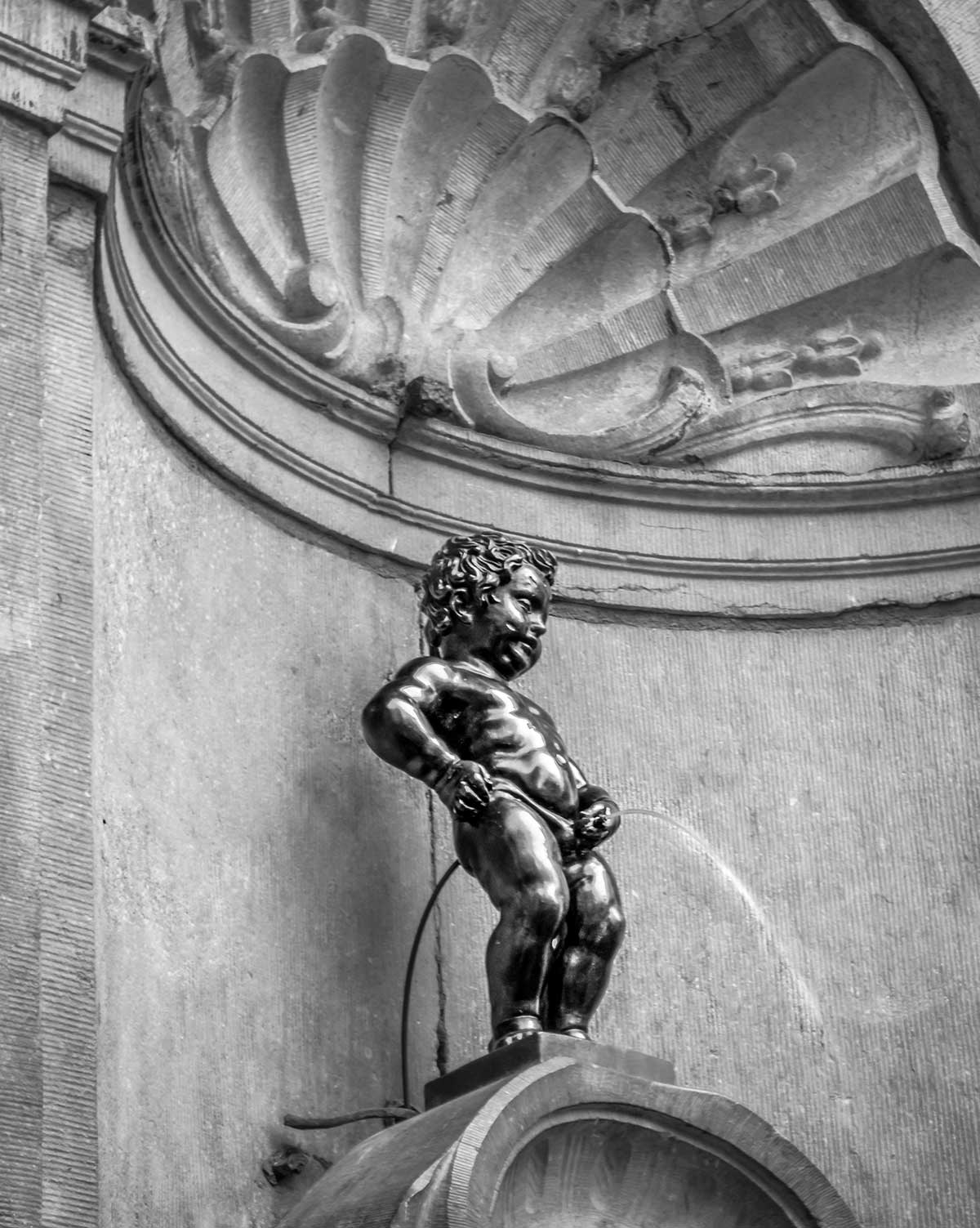 The Manneken Pis, a small bronze fountain sculpture in Brussels, depicts a naked boy urinating into the fountain's basin, serving as a whimsical and iconic landmark representing the city's playful spirit and historical charm.