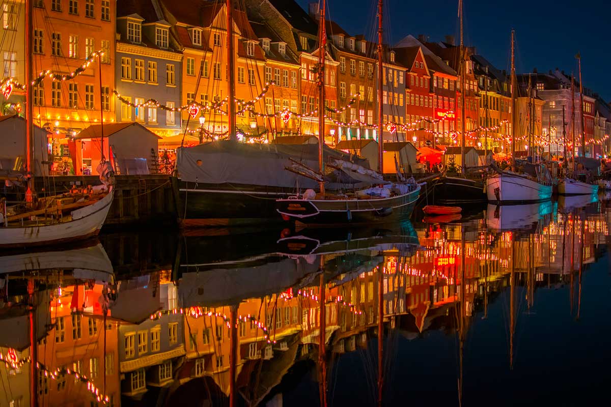 Nyhavn, Copenhagen's iconic harbor, features colorful 17th-century townhouses, historic wooden ships, and lively waterfront cafes, creating a picturesque scene reflecting the city's maritime heritage and vibrant atmosphere.