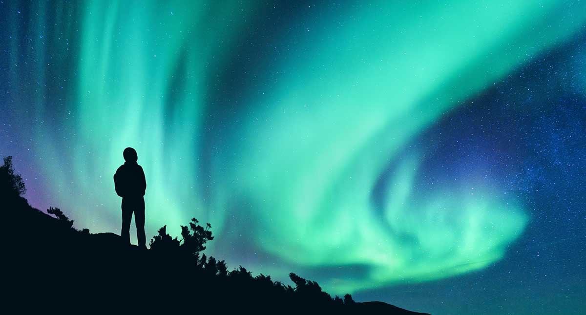 The Northern Lights, or Aurora Borealis, illuminate the Finnish sky with vibrant green, pink, and purple hues, a natural light display over snow-covered landscapes, attracting viewers to Lapland's winter wonderland.