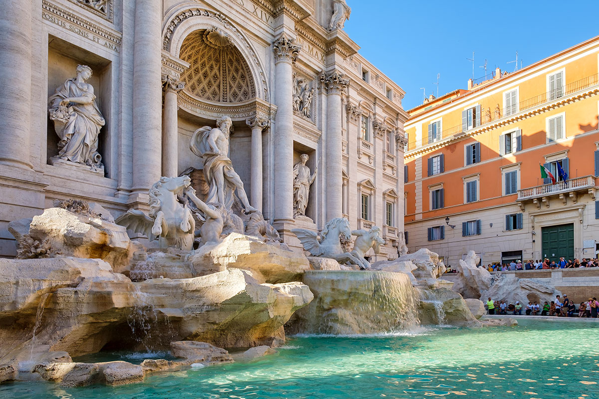 The Trevi Fountain in Rome, Italy, features a grand Baroque sculpture of Neptune surrounded by Tritons and sea horses, cascading water over intricate rockwork, and a bustling crowd of tourists, showcasing its iconic design and historical significance.