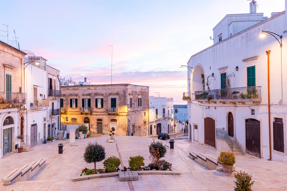 Ostuni, Apulia, Italy, features a hilltop "white city" with whitewashed buildings, narrow winding streets, and panoramic views of olive groves stretching to the Adriatic Sea, showcasing its picturesque landscape and historic charm.
