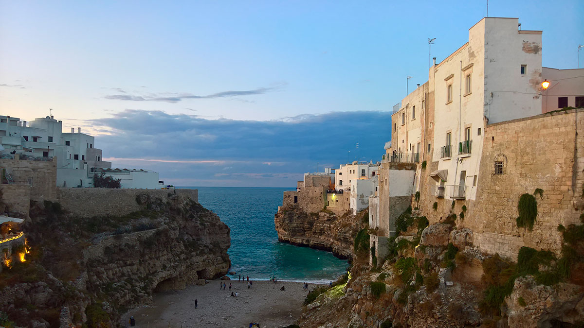 Polignano a Mare, Italy, features dramatic white cliffs overlooking the Adriatic Sea, a picturesque beach nestled between rocky outcrops, and historic buildings clinging to the seaside bluffs, showcasing its stunning coastal scenery and charming townscape.