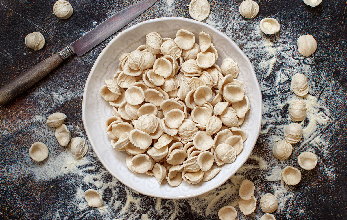 Fresh raw Italian pasta orecchiette, shaped like small ears, lies on a floured surface, showcasing its traditional handmade texture and preparation for a classic Apulian dish.