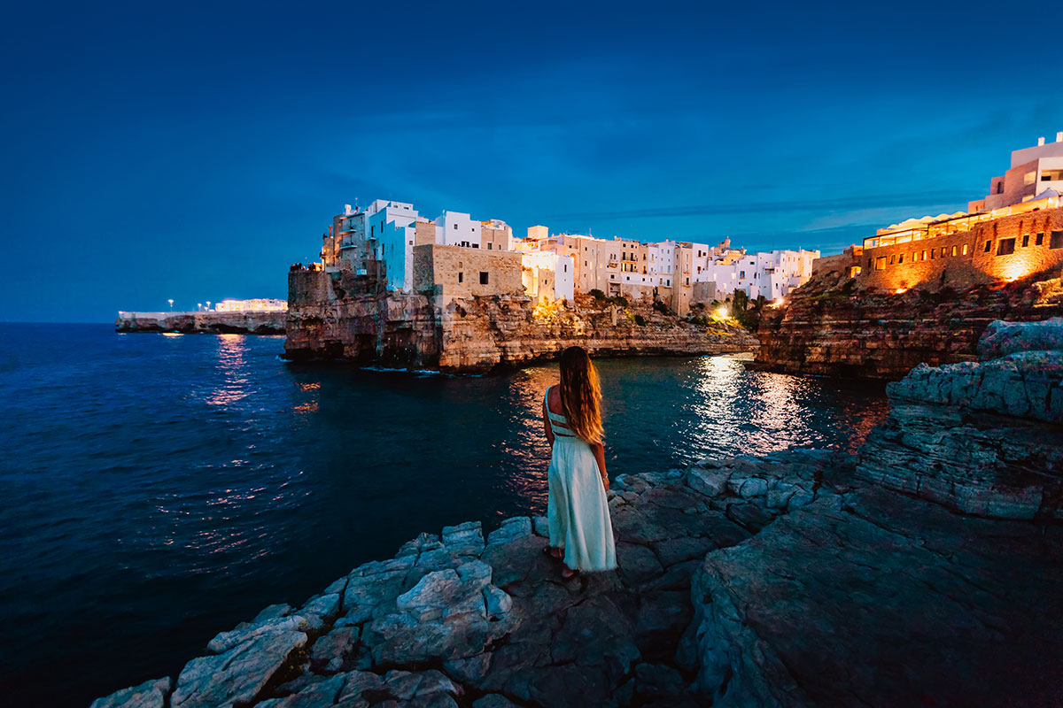 Polignano a Mare, Italy, features dramatic cliffs overlooking the Adriatic Sea, a small beach nestled in a cove, and historic buildings clinging to the rocky coastline, showcasing its picturesque seaside charm.