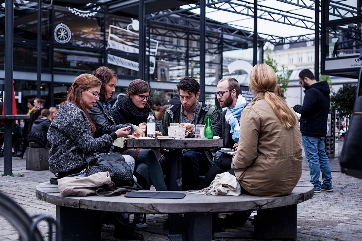 "Hygge" in Copenhagen is captured through warm lighting, cozy cafes with soft blankets, and people enjoying simple pleasures like coffee and conversation, illustrating the Danish concept of coziness and contentment permeating daily life.