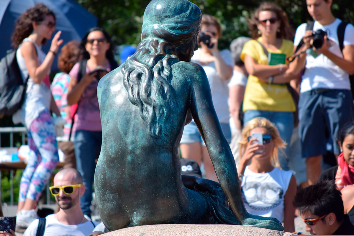 The Little Mermaid statue in Copenhagen, Denmark, depicts a bronze figure of a mermaid sitting on a rock by the harbor, showcasing the iconic sculpture inspired by Hans Christian Andersen's fairy tale and a popular tourist landmark.