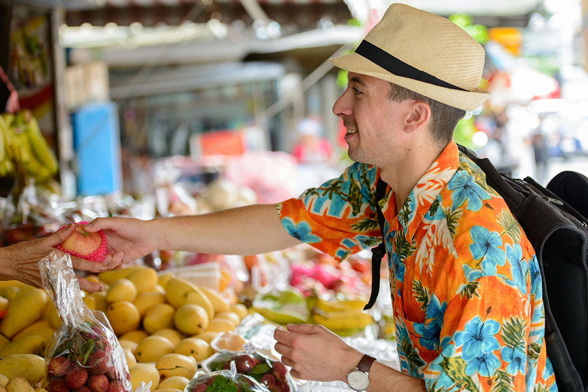 A traveler buying fresh, local produce at a market in Thailand
