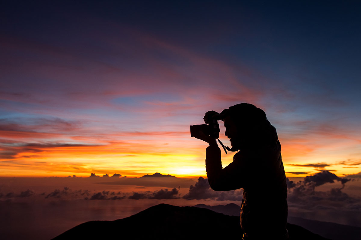 Traveler capturing a sunrise view with a DSLR camera on a mountaintop.