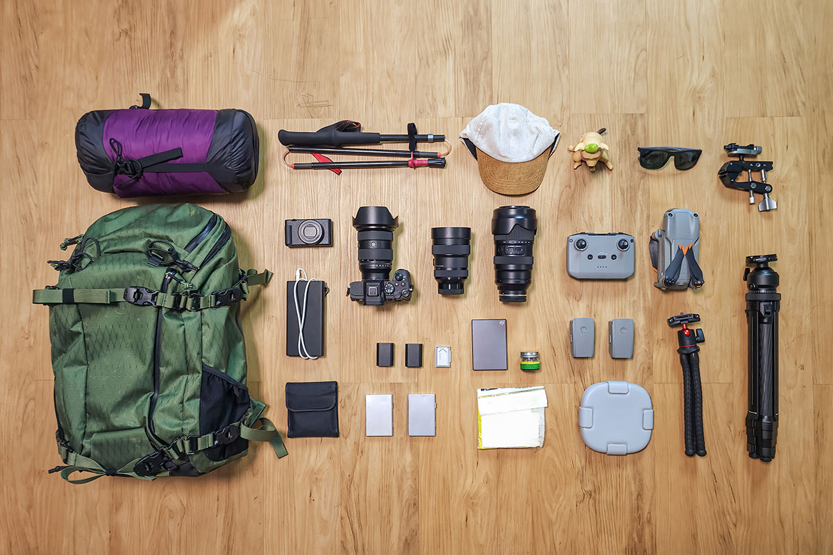 Flat lay of travel photography gear, including a camera, lenses, tripod, and memory cards.