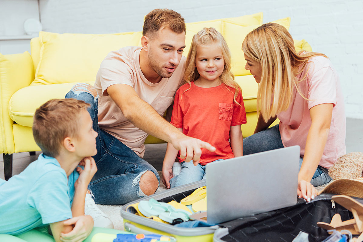 A family sitting on a couch, happily browsing travel options on a laptop.