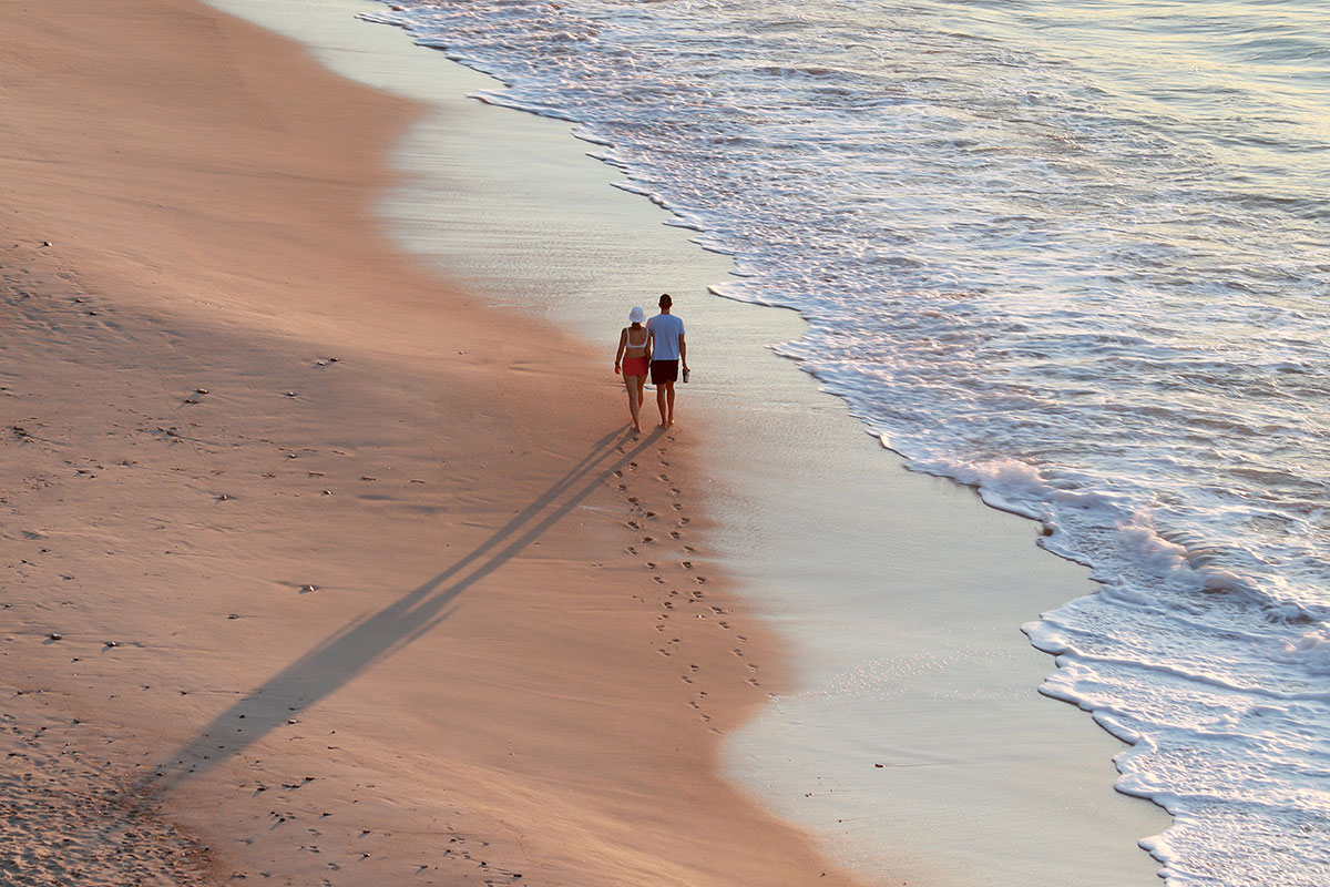 A couple walking hand-in-hand on a secluded beach in the Algarve at sunset.