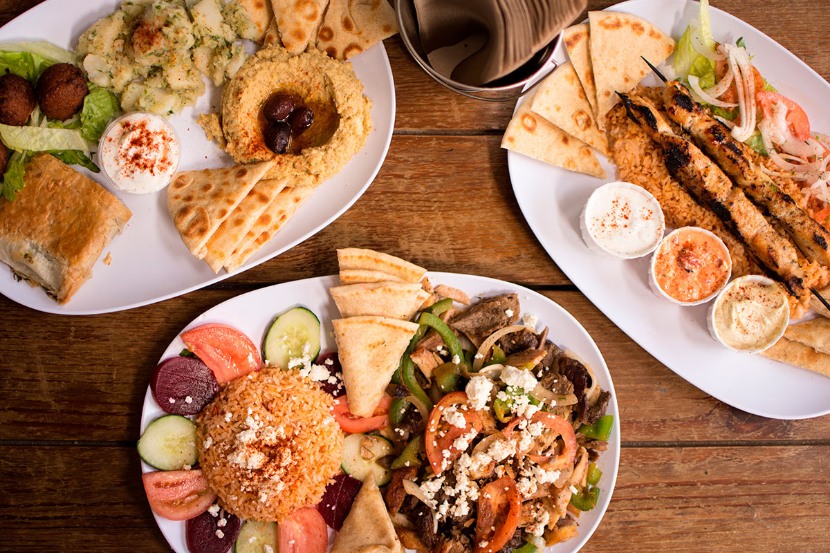 A table set with Greek dishes including moussaka, souvlaki, and a Greek salad