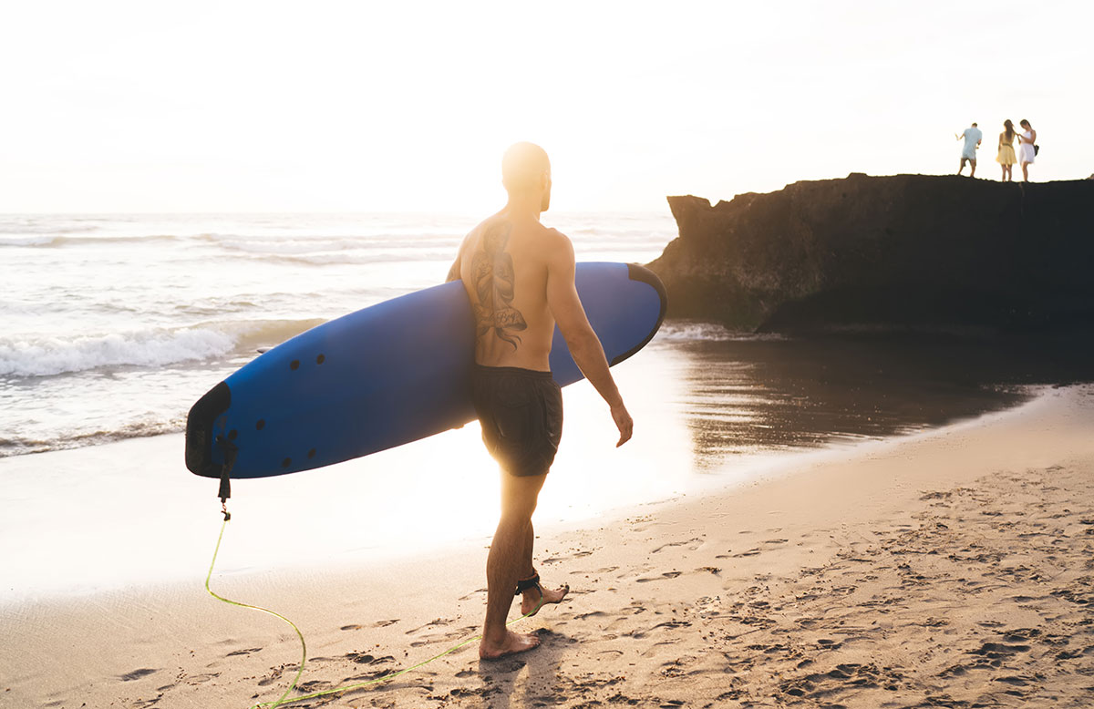 Surfer walking along the beach at sunset in Canggu