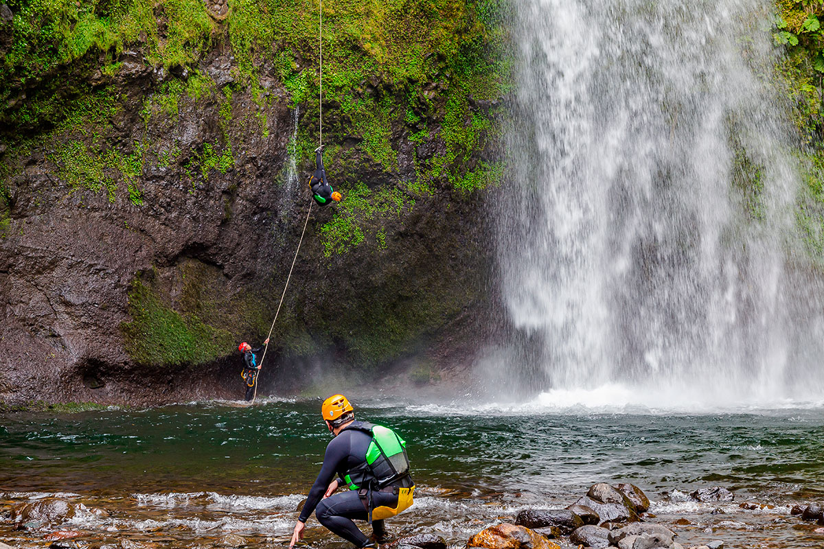 A canyoning guide helping a tourist rappel down a waterfall in Madeira