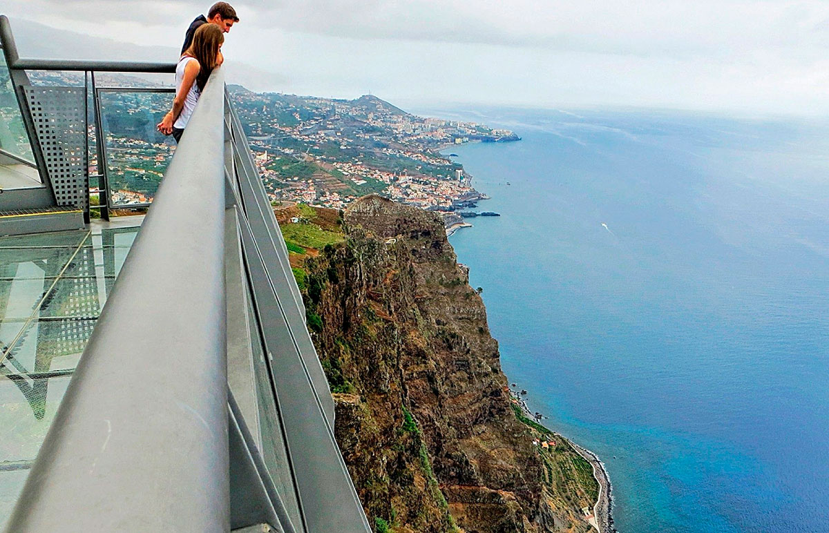 Tourists standing on Cabo Girão glass skywalk overlooking the ocean