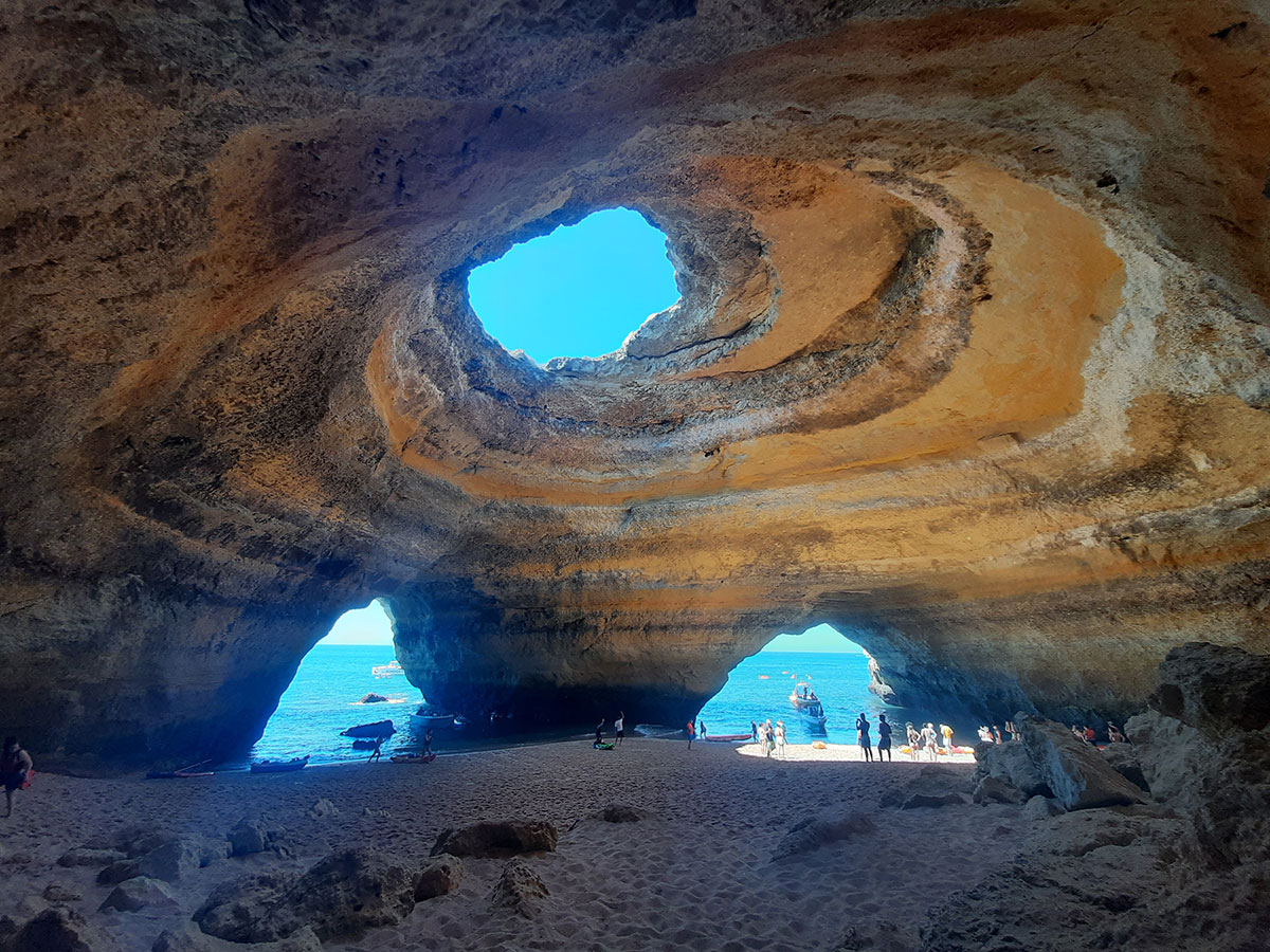 Interior view of Benagil Cave with sunlight streaming through the ceiling opening.​