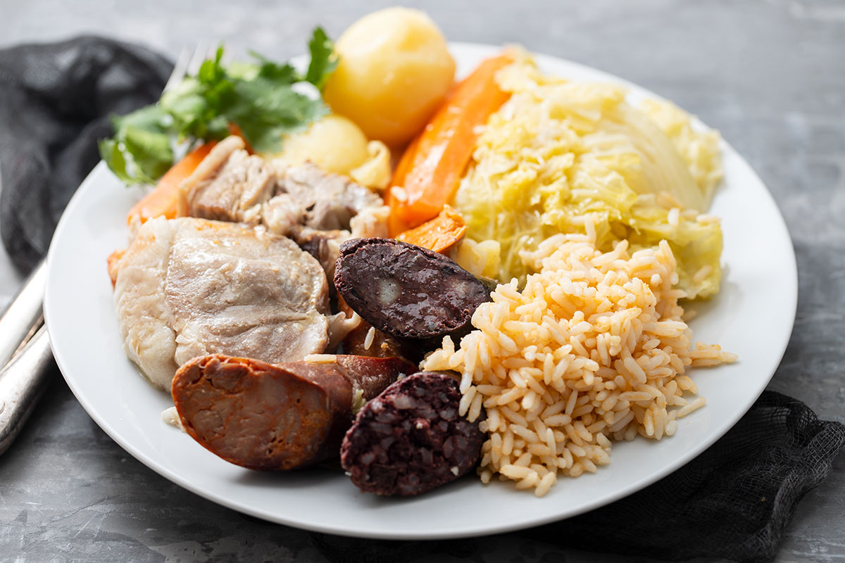 Traditional Portuguese dish "cozido à portuguesa" served with a hearty mix of meats, vegetables, and sausages on a rustic ceramic plate.