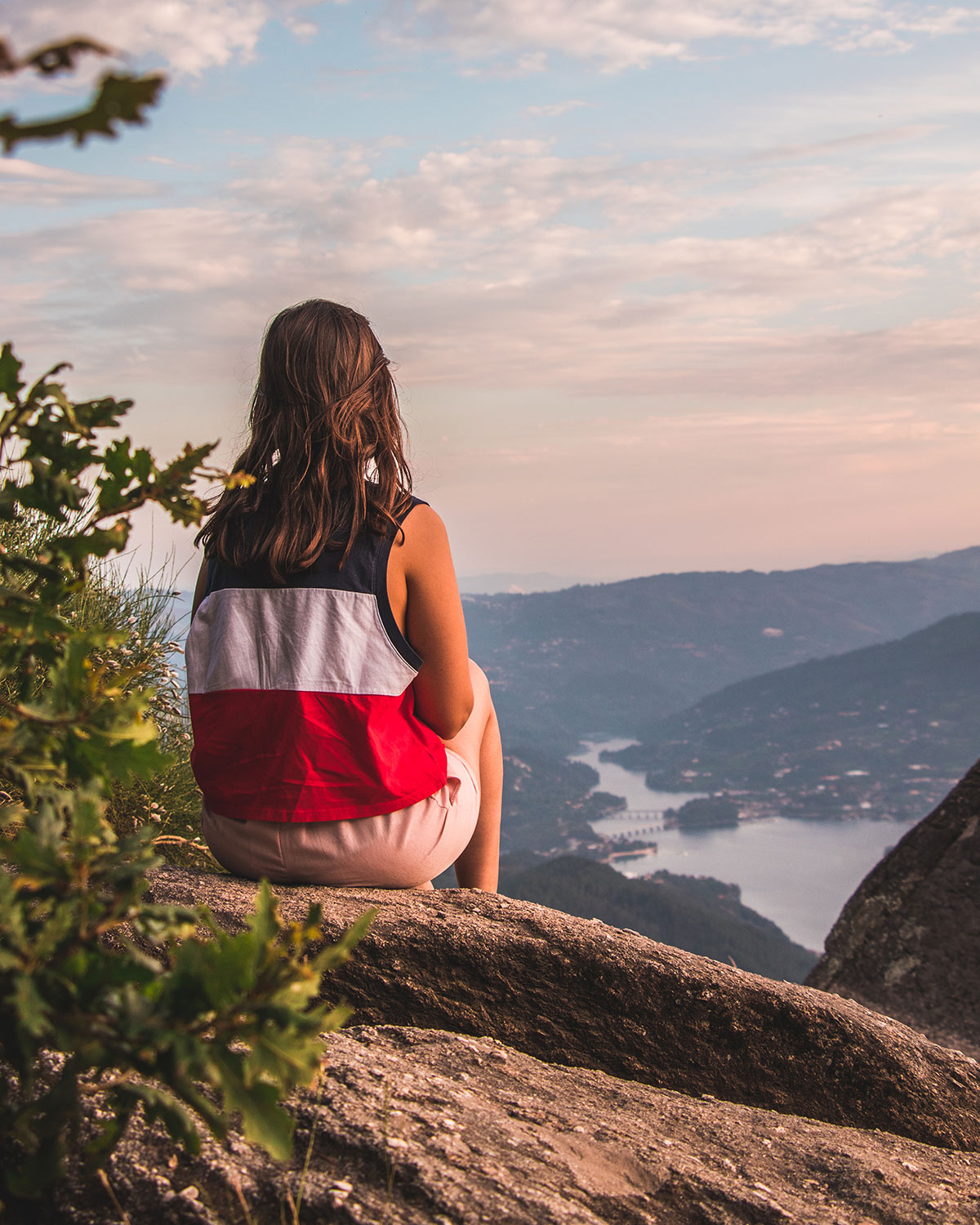Young woman sitting on a rock, gazing at the majestic mountain landscape with a shimmering dam lake in the background in Peneda-Gerês National Park.