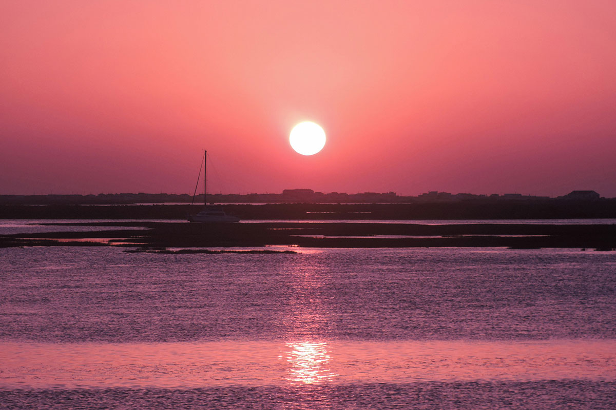 A small boat gliding through the golden waters of Ria Formosa at sunset, leading into a magical night of stargazing under a clear sky.