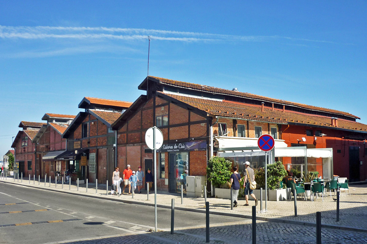 Vibrant view of Cais do Sodré waterfront with colorful buildings, cafés, and the Tagus River in the background.