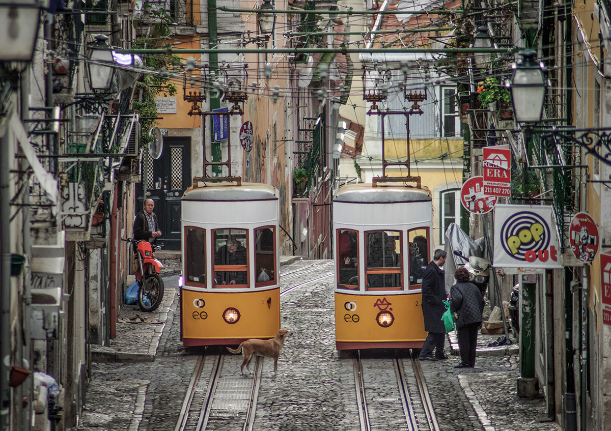 Historic yellow Elevador da Bica tram climbing a steep, narrow street lined with colorful buildings in Lisbon.