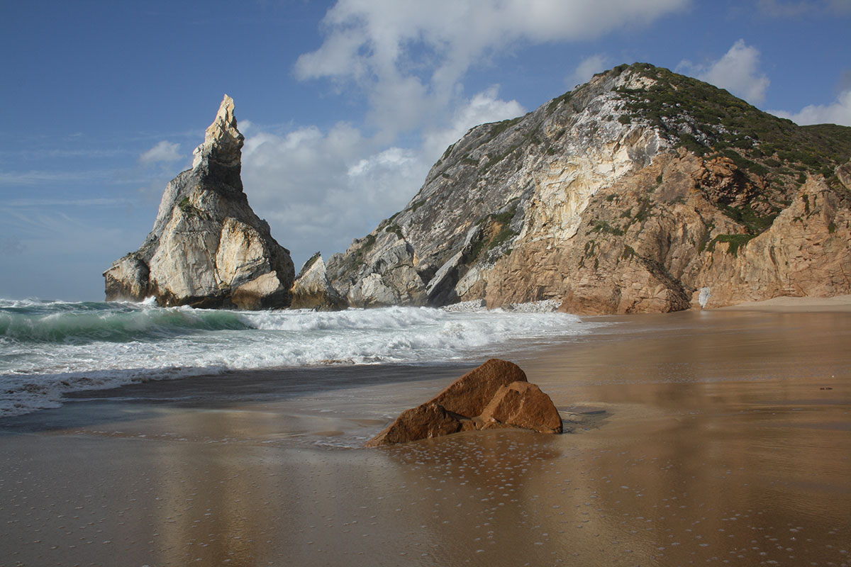 Dramatic view of Praia da Ursa with rugged cliffs, golden sand, and turquoise waves crashing against sea stacks near Sintra.