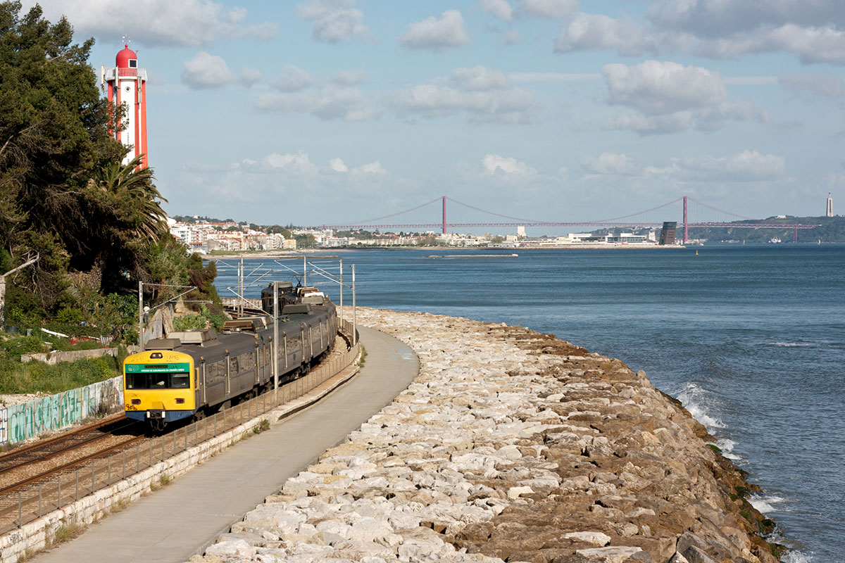 Train on the Linha de Cascais traveling along the scenic coastline between Lisbon and Cascais, with ocean views and rocky cliffs.