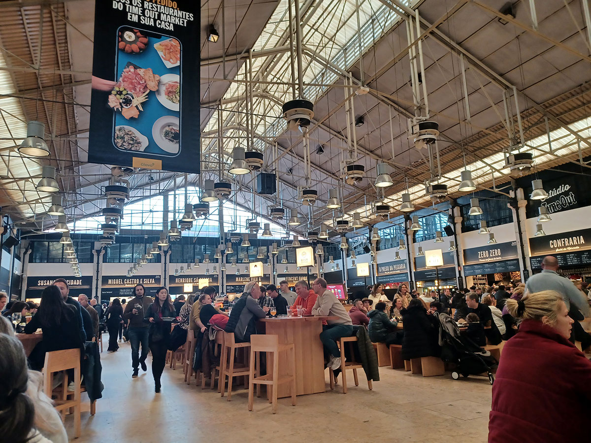 Bustling interior of the Ribeira Market food hall in Lisbon, with communal seating, gourmet food stalls, and vibrant crowds enjoying local cuisine.