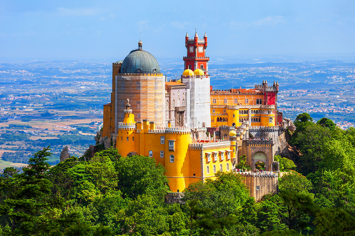 Colorful and eclectic architecture of Palácio da Pena perched on a hilltop in Sintra, surrounded by lush forest.