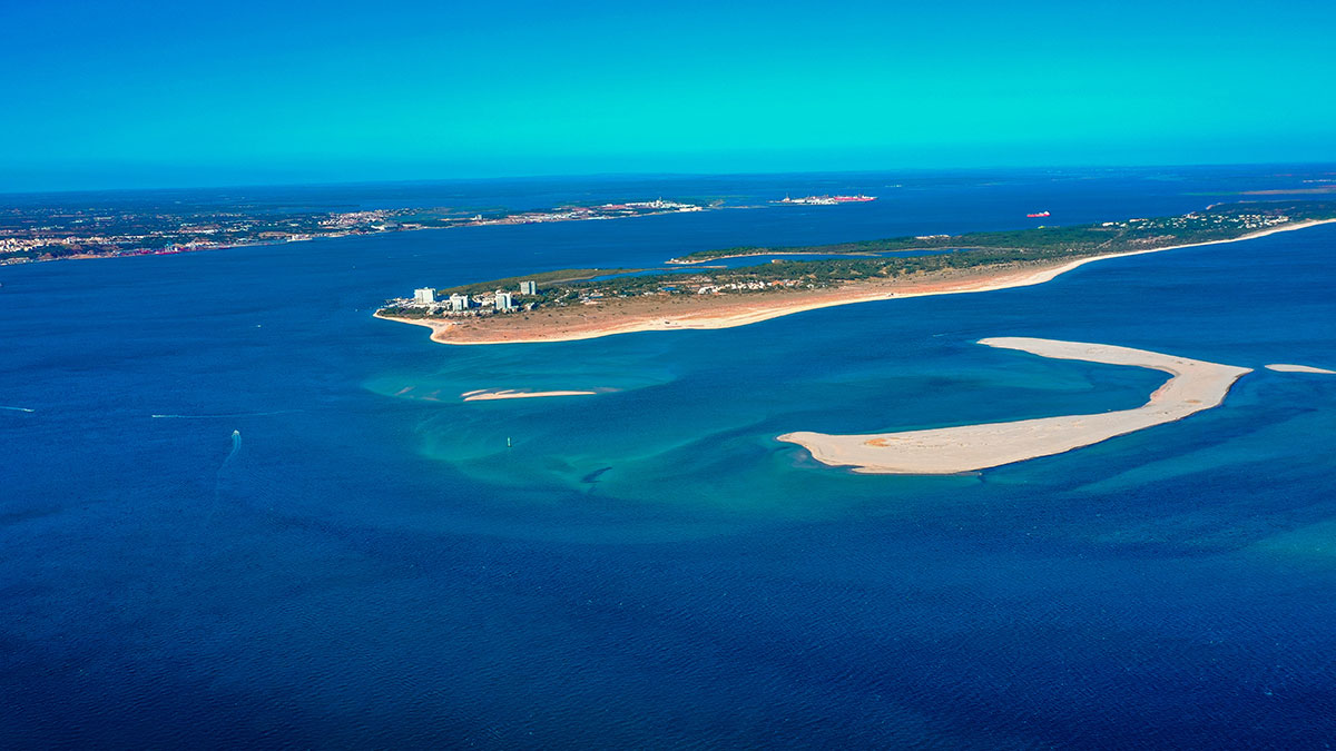 Aerial view of the Tróia Peninsula with turquoise waters, white sandy beaches, and lush greenery stretching between the Atlantic Ocean and the Sado River.