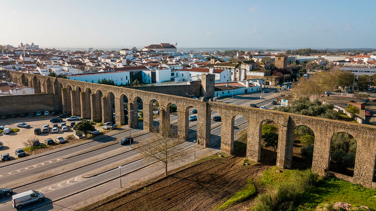 A narrow cobblestone street in Évora intersected by the ancient Água de Prata aqueduct.