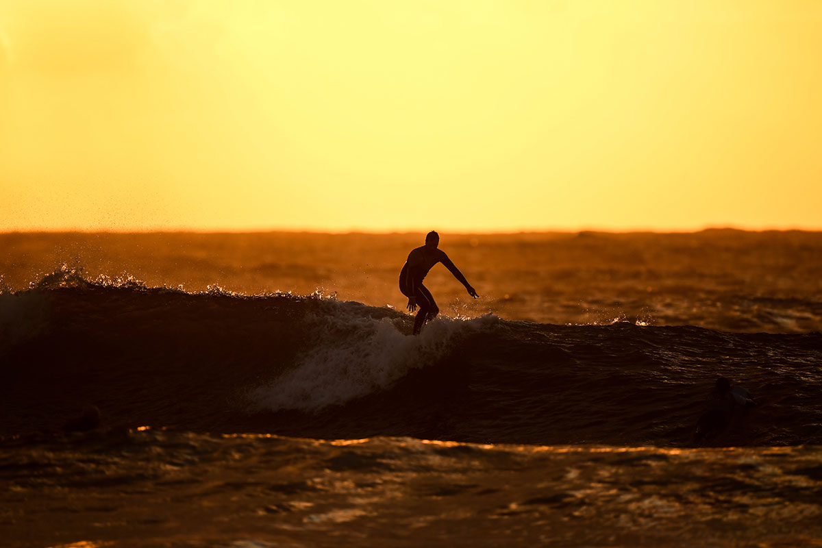 Surfer silhouetted against a vibrant ocean sunset at Ericeira World Surfing Reserve