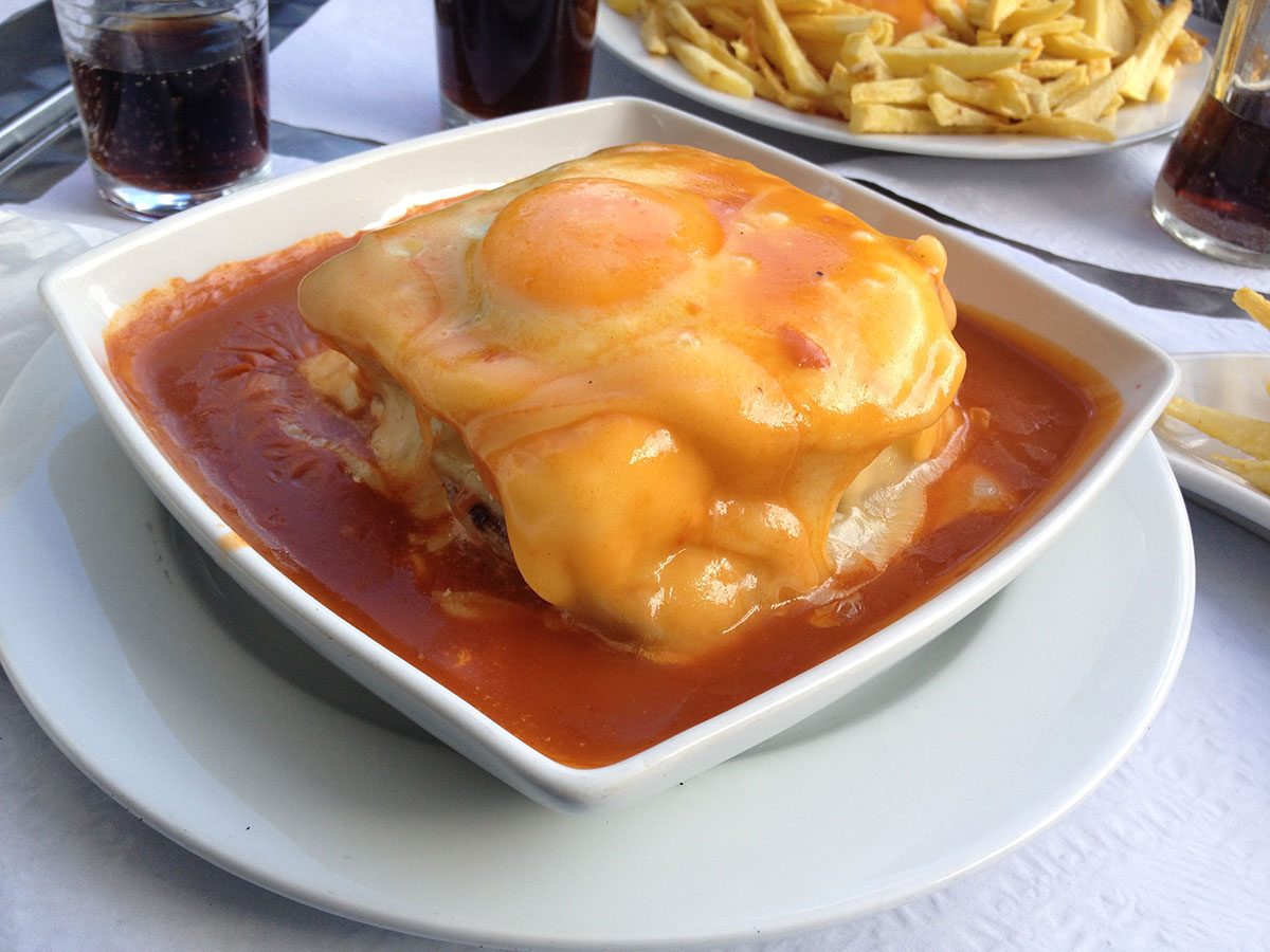 Traditional Francesinha sandwich topped with melted cheese and sauce