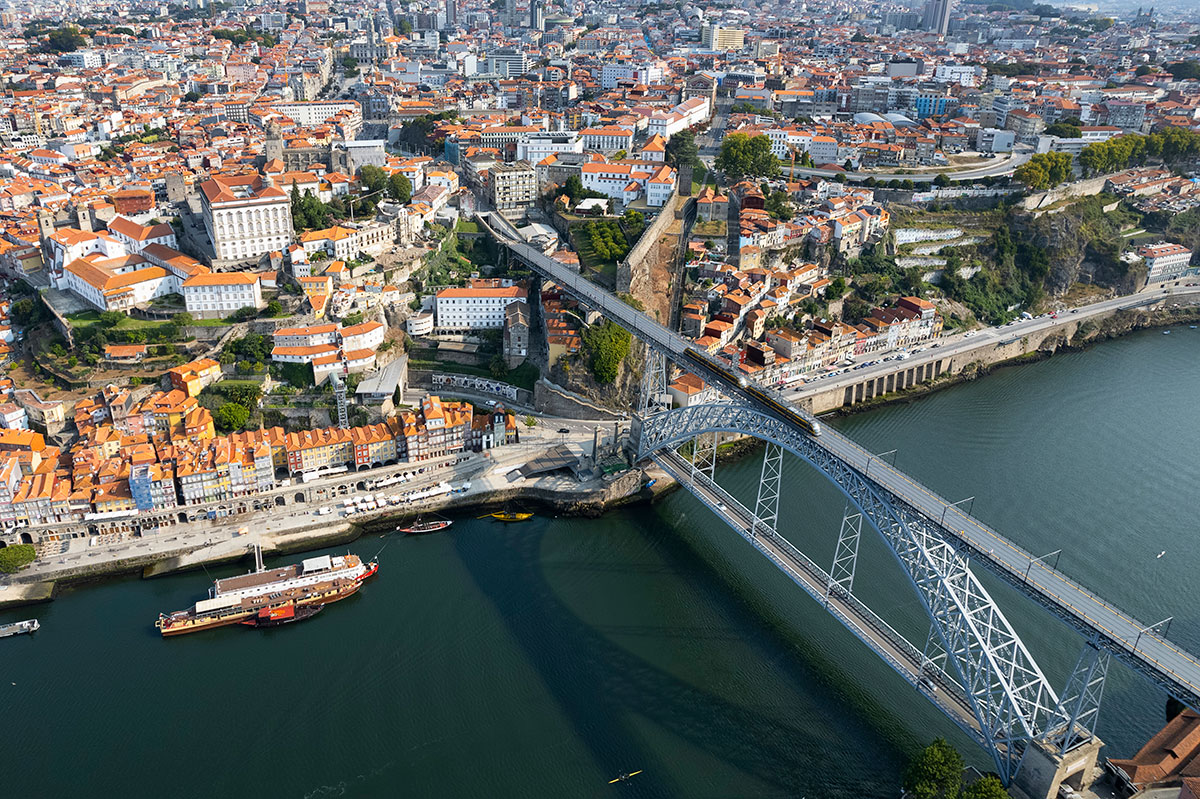 Aerial view of Porto with the Douro River winding through the city, historic Ribeira district, and Dom Luís I Bridge visible from above.