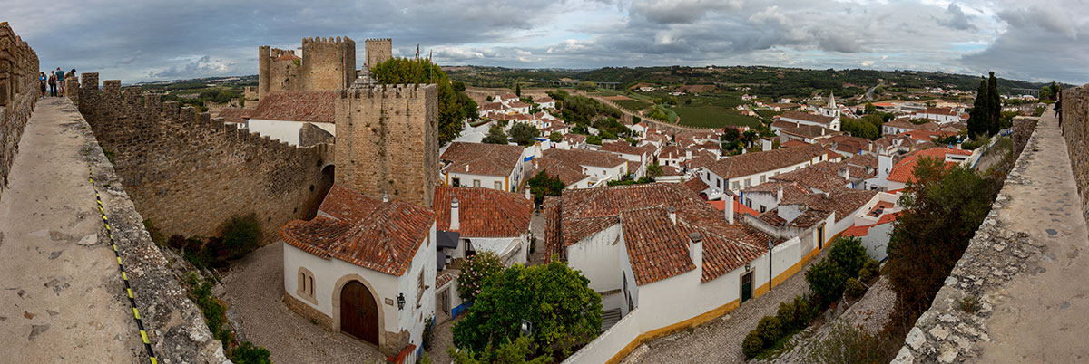 Aerial view of the walled medieval town of Óbidos, Portugal, showcasing its terracotta rooftops and surrounding countryside.