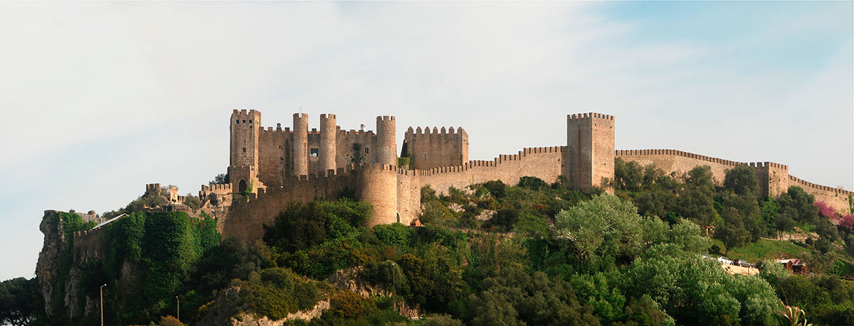 Tourists walking along the stone castle walls of Óbidos, with views of the town below.