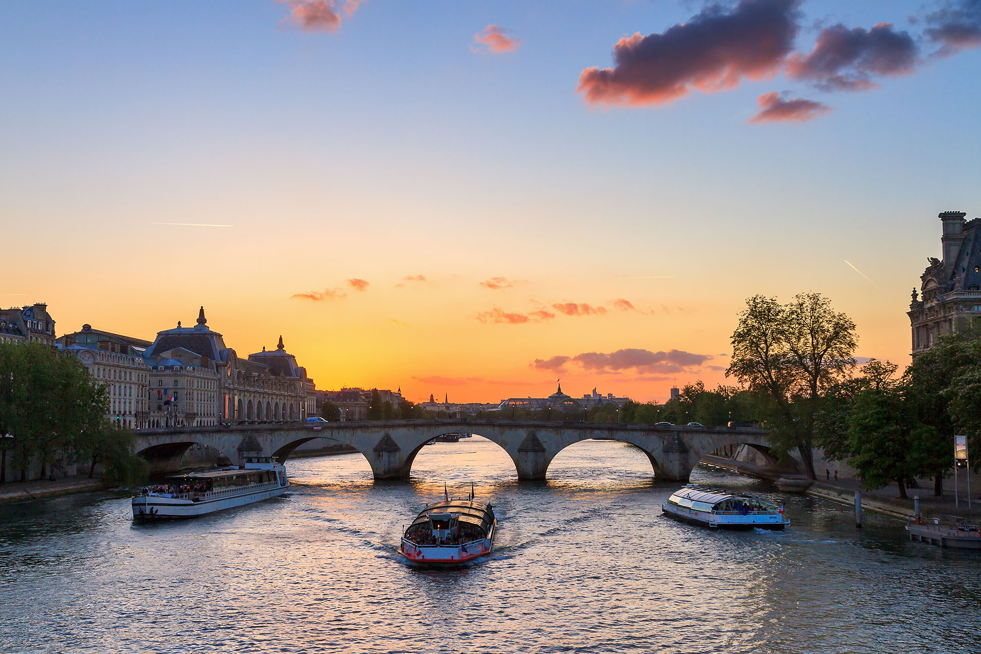 Beautiful vibrant sunset over the river Seine in Paris, France, with a tourist canalboat under an arched bridge and the Grand Palais in the background
