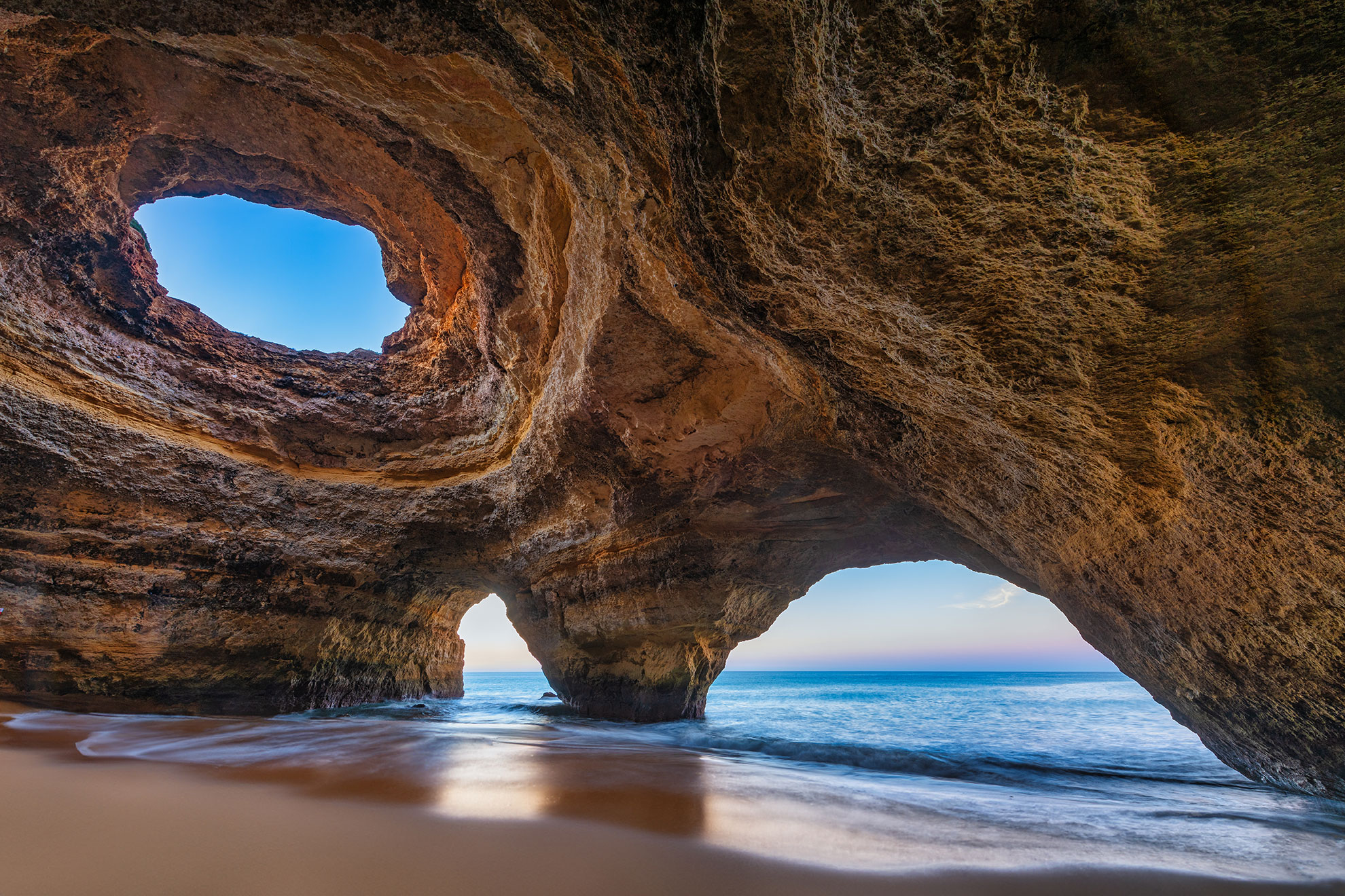 Inside Benagil Cave, Algarve — golden sandstone dome with circular skylight open to blue sky, turquoise water below
