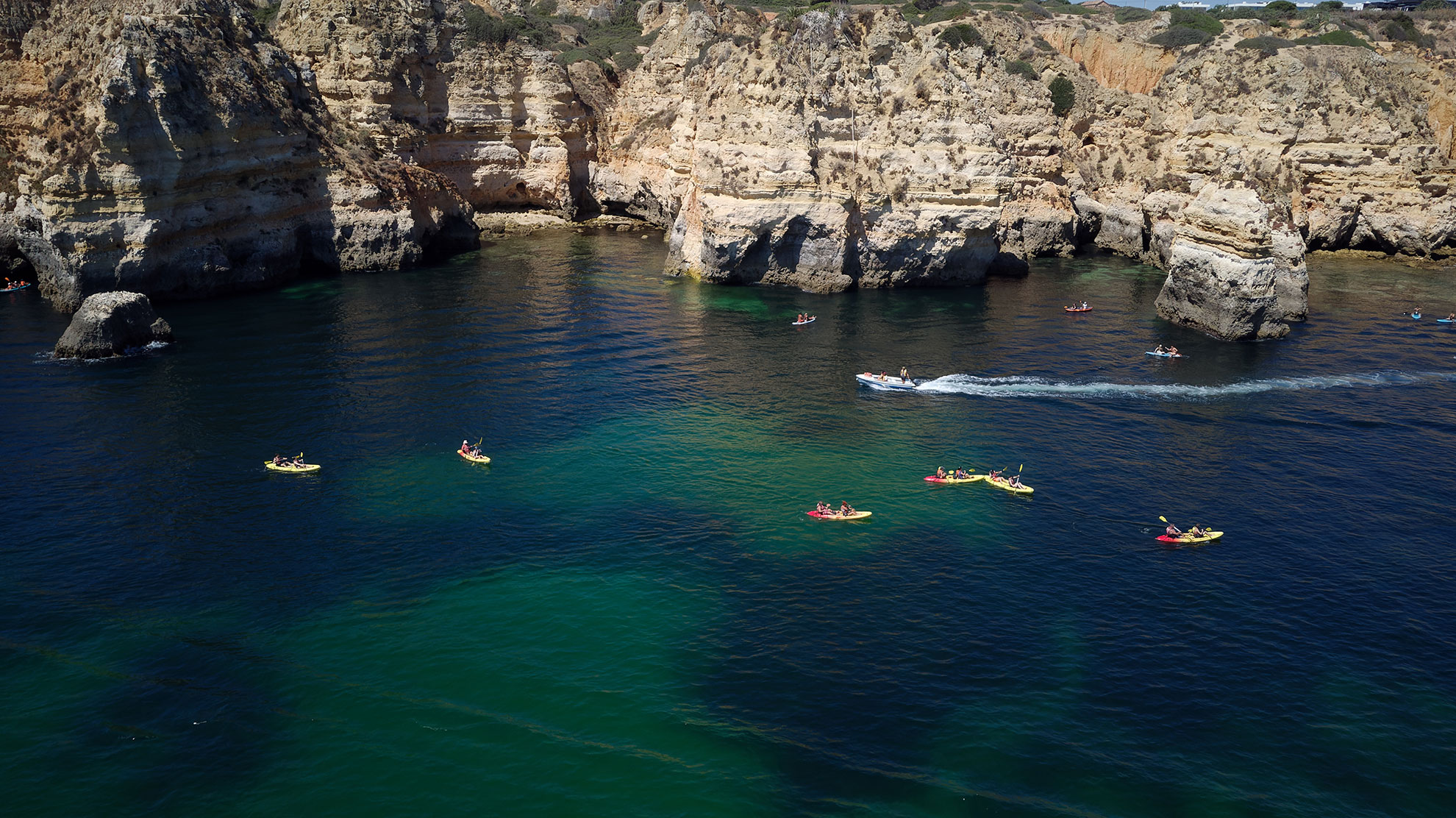 Aerial view of kayakers paddling turquoise waters between golden limestone sea caves along the Algarve coast near Benagil